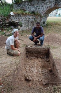 Lynsey Bates (l) and Krystle Edwards (r), DAACS staff, at Units 1 and 3 at the Papine Village. Note the cobble surface likly built to control muddy conditions around the cistern. The cistern and aqueduct are in the background. Photogaphed in 2009.